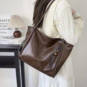 Detalle del bolso tote de cuero marrón oscuro con colgante de campana y costura lateral
