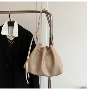 Detailed close-up of beige drawstring bucket bag with pleated leather and knotted strap