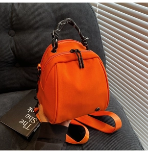Detail of bright orange mini nylon shell backpack with woven handle and circular metal logo