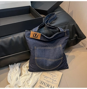 Close-up of denim tote bag with brown leather patch and curved stitching pocket details