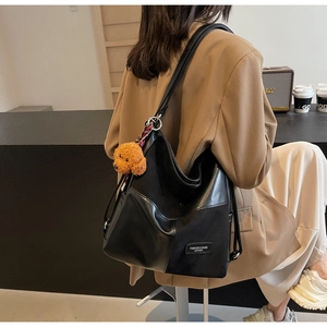 Detail of black leather hobo bag with fashion logo and brown puppy plush pendant charm