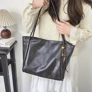 Detalle de un bolso tote negro mate grande con colgante de llave dorada en un ambiente interior