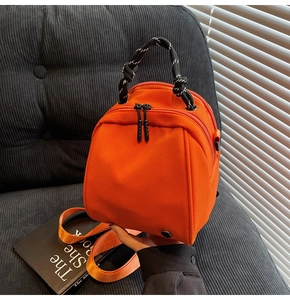 Detail of bright orange nylon mini backpack with a black and white braided handle and strap