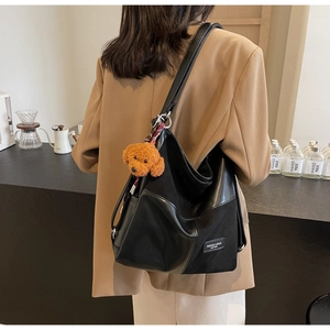 Detail of a black patchwork tote bag featuring a plush bear charm and side leather label