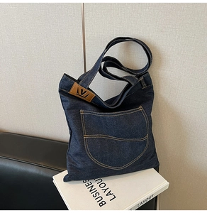Close-up of deep blue denim tote bag featuring white contrast stitching and a side leather logo