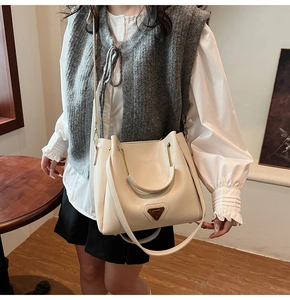 Détail du sac seau en cuir PU crème avec poignées dorées en U et ornements métalliques