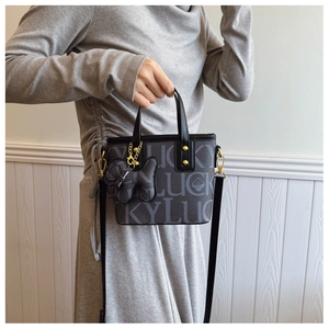 Detail der Crossbody-Tasche mit LUCKY-Druckmuster und schwarzem Hund-Anhänger
