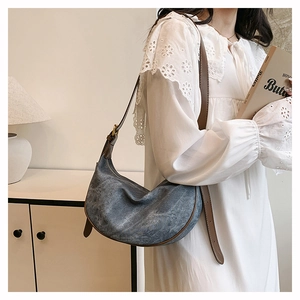 Detail of blue denim crescent bag with dark brown leather straps and gold buckle adjustment