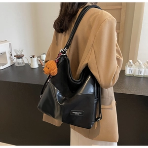 Detail of black leather tote bag with patchwork design and brown teddy bear charm