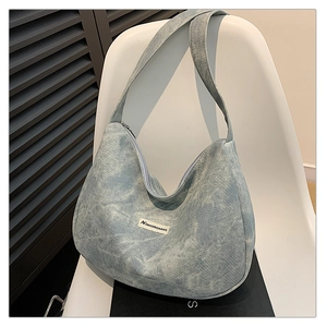 Close-up of a light blue washed denim crescent bag hanging on a white chair detail