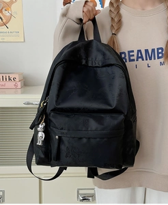Detail of black embossed backpack featuring a front zipper pocket and silver bear pendant