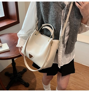 Détail d'un sac seau crème chic avec poignée en métal doré et plaque métallique signée