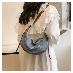 Detail of denim crossbody bag with brown leather strap worn with white lace dress