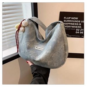 Detail of light blue denim crescent bag with red woven charm and plush pompom accessory