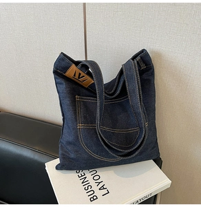 Detail of blue denim tote bag with yellow contrast stitching and leather brand logo label