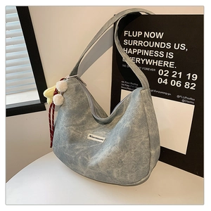Detail of light blue denim hobo bag with a star charm and branded patch on a white table