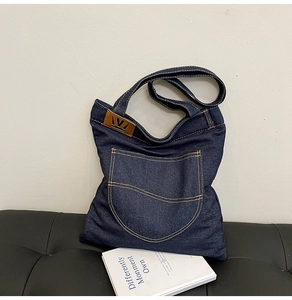 Macro detail of dark blue denim tote bag with yellow stitching and leather logo