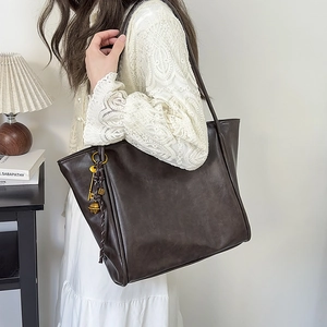 Primer plano de bolso tote de cuero marrón oscuro con colgantes vintage colgado al hombro