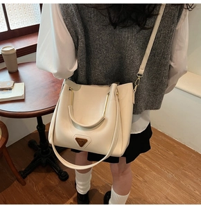 Détail du sac seau crème avec logo triangulaire en métal et poignée chic dans un café