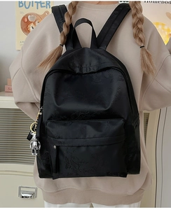 Detailed view of black nylon backpack with bamboo leaf pattern and robot pendant charm