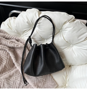Close-up of black lychee grain leather bucket bag with drawstring and metal ball detail