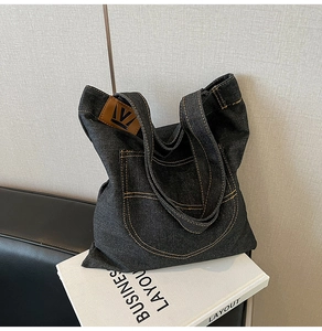 Detail of dark grey denim tote bag with orange stitching and leather logo patch