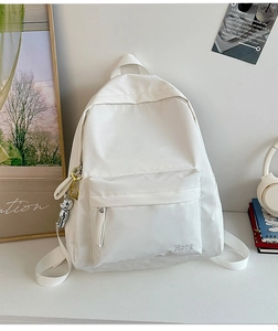 Detailed view of the white canvas backpack with a cute silver bear charm and embroidery