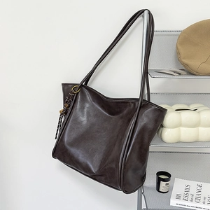 Detalle de un bolso tote de cuero mate marrón oscuro con un colgante de borla tejida
