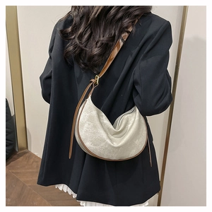 Model wearing a minimalist cream dumpling crossbody bag with brown leather shoulder strap