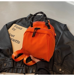 Detail van een feloranje nylon mini-rugzak met zwart-wit geweven handvat voor dames