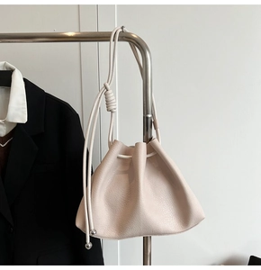 Detail of a beige drawstring bucket bag featuring silver metal beads and leather texture