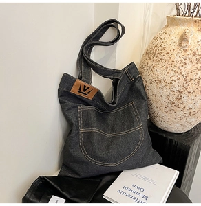 Detail of the brown leather logo patch on a black denim tote bag with visible stitching