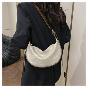 Detail of a beige crescent crossbody bag with brown trim and metallic adjustment buckle