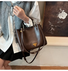 Détail du sac seau en cuir marron foncé avec anse dorée circulaire et logo en métal