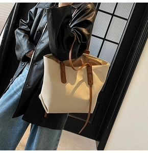 Detail of beige canvas tote bag with brown leather straps worn by model in city setting