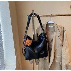 Detail of black PU leather tote bag with brown plush puppy charm and woven tassel