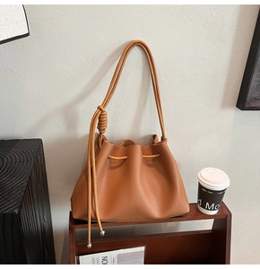 Detailed close-up of brown pebbled leather bucket bag with braided knot and silver metal ball