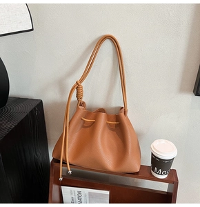 Close-up of caramel leather bucket bag with pleated texture and silver ball metal charm