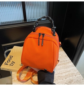 Detail of vibrant orange shell mini backpack with woven handle on stone surface