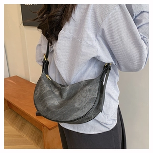 Detail of grey crescent crossbody bag with adjustable strap worn by model against a wall