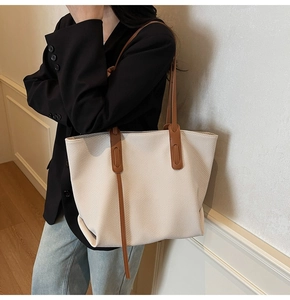 Detail of a large cream woven tote bag with brown leather handles and side straps