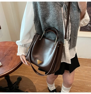 Détail du sac seau marron foncé avec logo triangle en métal et design à double sangle