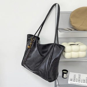Detalle de un bolso tote negro grande con correas largas y colgante metálico decorativo