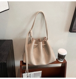 Detail of minimalist cream bucket bag featuring drawstring closure and knotted leather strap