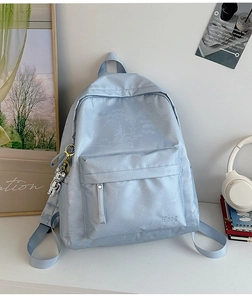 Detail of light blue nylon backpack with leaf patterns and silver bear charm accessory