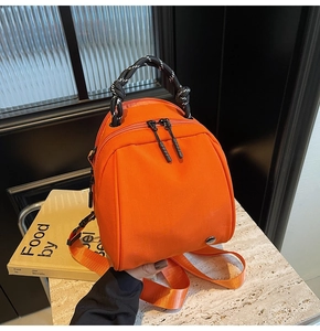 Detail of a bright orange mini shell backpack with braided handles and silver metal logo