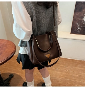 Détail du sac seau marron foncé avec poignée en métal doré et garniture métallique