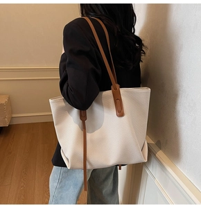 Detail of off-white woven tote bag with brown leather straps worn on shoulder