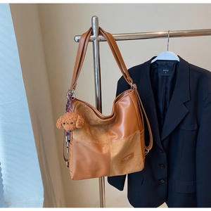 Detail of brown tote bag featuring mixed leather textures and plush puppy charm accessory