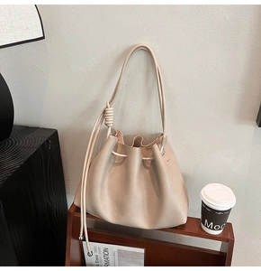 Detail of a beige drawstring bucket bag with litchi grain texture on a dark wooden shelf
